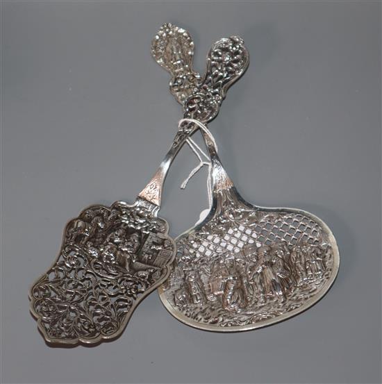 Two late 19th century Dutch white metal gateau serving spoons, pierced and embossed with figures